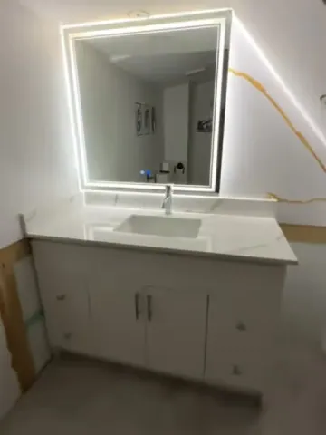 Illuminated mirror and white vanity beside a gold-veined tiled wall