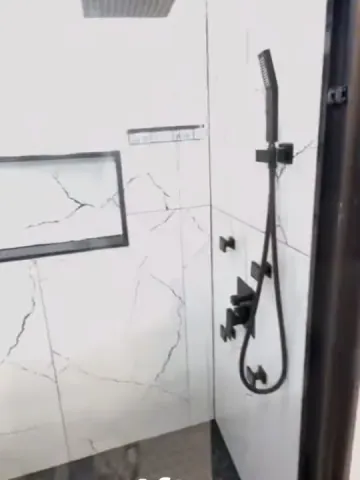 Black shower fittings and a recessed niche against white veined tiles
