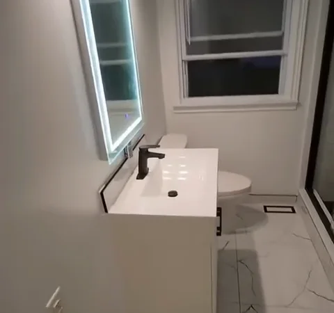After renovation: white vanity, illuminated mirror and marble-look floor tiles