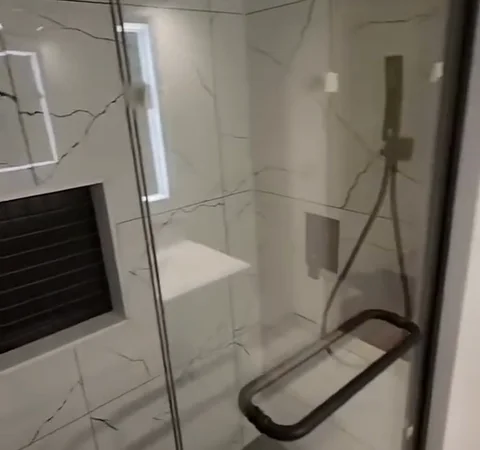 Finished glass shower with marble-look wall tile, dark fittings and a recessed niche