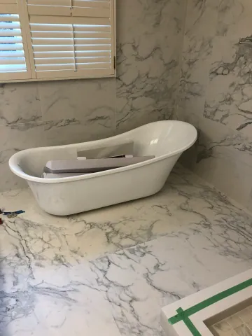 Freestanding bathtub beside a window and marble-look tiled walls
