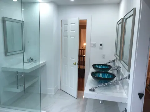 Marble-look bathroom with a glass shower and blue glass vessel sinks