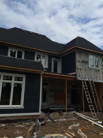 Home addition with dark siding and large windows during exterior finishing