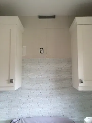 Wall tile installation between white kitchen cabinets