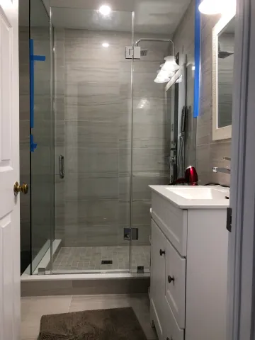 Compact tiled bathroom with a glass shower and white vanity