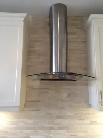 Stainless-steel range hood above a stone tile backsplash